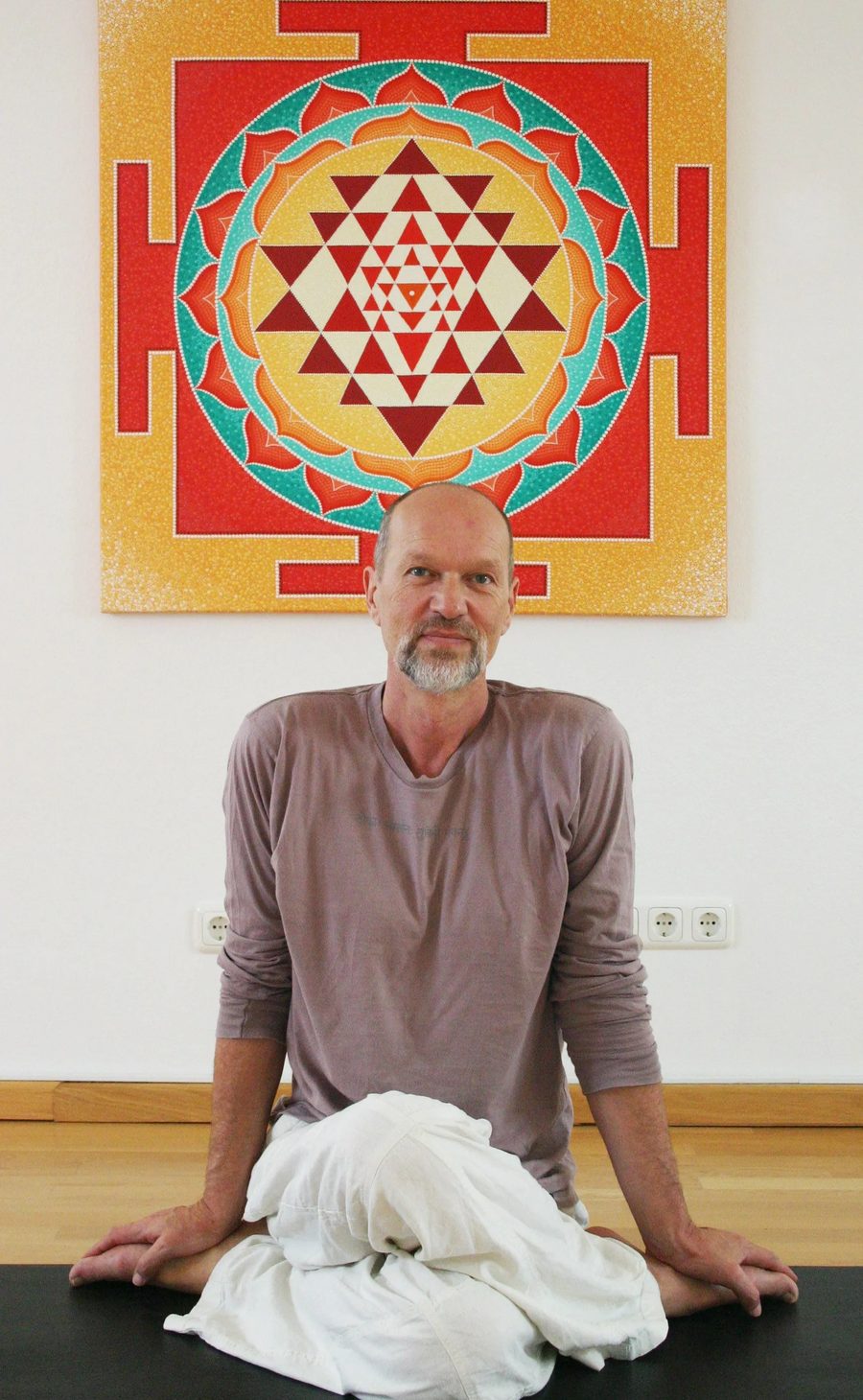 Vikram sitzt vor einem großen Shri-Yantra in Rot, Gold und Türkis